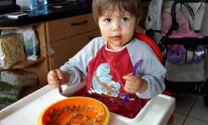 Foto eines Tageskindes mit verschmiertem Gesicht beim Essen des frisch zubereiteten Mittagessens.